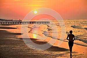 Silhouette of young man running on beach sand at sunrise. Original wallpaper from summer active vacation