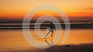 Silhouette of young man runs along the beach during amazing sunset.