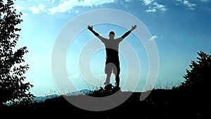 Silhouette young man runs up to top of mountain and uplifts his hands as a sign of achievement, success and joy. Concept