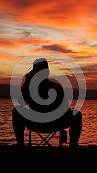 Silhouette of a young man sitting by the lake enjoying the sunset