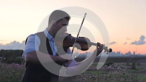 Silhouette young man of a violinist in the field at sunset playing the violin