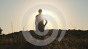 Silhouette of Young Man Walking in Field to Setting Sun and Raising Hands Up