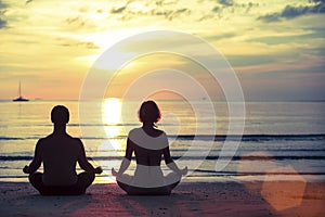 Silhouette of young man and woman practicing yoga in the lotus position on the ocean beach.