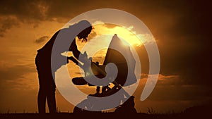 Silhouette of young mother with a baby stroller enjoying motherhood at sunset. Young woman looking at child in baby