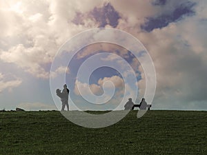 Silhouette of young and old couple against bright cloudy sky. Young pair standing and holding each other in their hands. Older