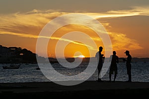 Silhouette of young people jumping from the Crush bridge at the yellow sunset on Ribeira beach in Salvador (BA