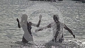 The silhouette of young people of the man and woman who stand in the sea and splashes water hands,slow motion