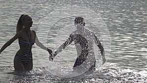 The silhouette of young people of the man and woman who stand in the sea and splashes water hands,slow motion