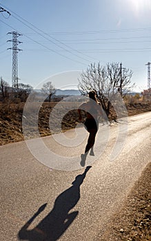 Silhouette of a young retro runner woman illuminated by dawn sunlight, running stylishly suspended in the air on a paved path of a