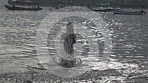 The silhouette of the young slender happy woman who stand in the sea and splashes water hands.slow motion