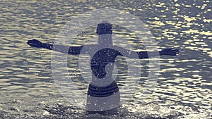 The silhouette of the young slender happy woman who stand in the sea and splashes water hands.slow motion