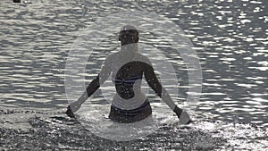 The silhouette of the young slender happy woman who stand in the sea and splashes water hands.slow motion