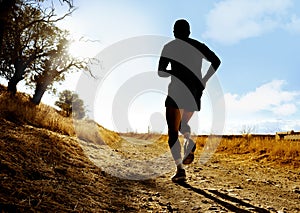 Silhouette of young sport man running on countryside in cross country workout at summer sunset