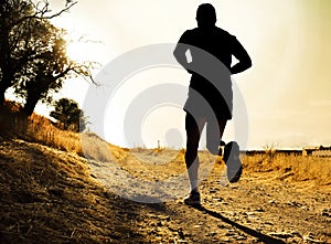 Silhouette of young sport man running on countryside in cross country workout at summer sunset