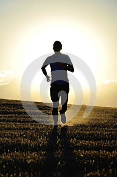 Silhouette young sport man running off road in countryside straw field backlight at summer sunset photo
