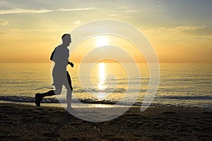 Silhouette young sport man running outdoors on beach at sunset with orange sky