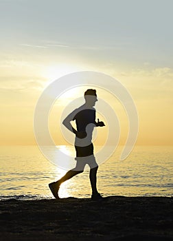 Silhouette young sport man running outdoors on beach at sunset with orange sky