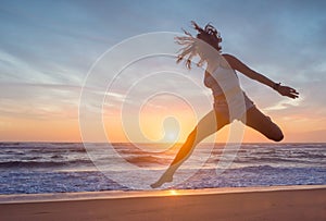 silhouette of a young sporty woman jumping on the beach at sunset