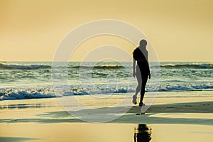 Silhouette of young sporty woman walking on seashore after running workout at a beautiful beach enjoying sunset light and relax in