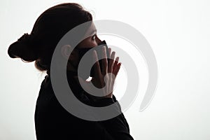 Silhouette of young woman in black protective mask covering face on studio background, scared girl looking horrified, concept of