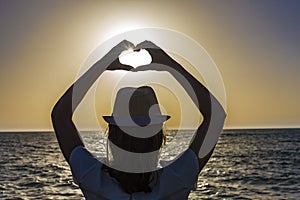 Silhouette of a young woman creating the shape of a heart with her hands with the sun nearly inside