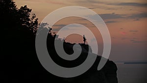 Silhouette of young woman dancing on top of a cliff by the river at sunset