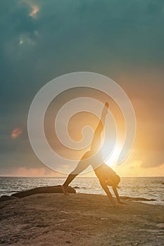 Silhouette young woman does yoga position splits or twine for healthy lifestyle on tropical coast sea