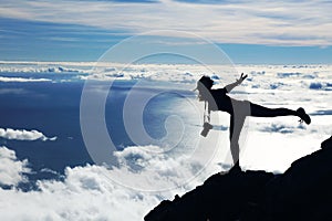 The silhouette of a young woman doing balance on Pico volcano. Contre-jour photographic technique.