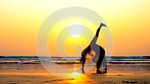 Silhouette of young woman doing gymnastic bridge on the beach