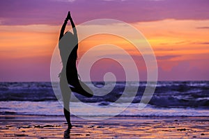 Silhouette young woman doing yoga on the beach at sunset