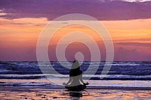 Silhouette young woman doing yoga on the beach at sunset