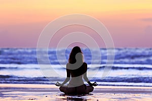 Silhouette young woman doing yoga on the beach at sunset