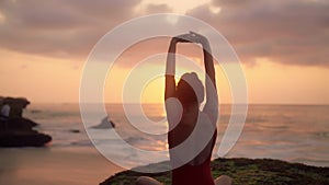 Silhouette of young woman doing yoga exercises. Girl in red swimsuit relaxing on the ocean coast. Pretty brunette woman
