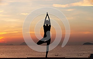 Silhouette of a young woman doing yoga near the sea at sunset