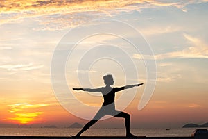 Silhouette of a young woman doing yoga near the sea at sunset