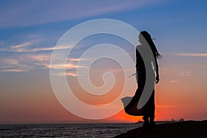 Silhouette of young woman in dress standing by the sea