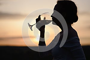 The silhouette of a young woman drinking wine in a sunset