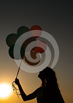 Silhouette of young woman with flying balloons against the sky.
