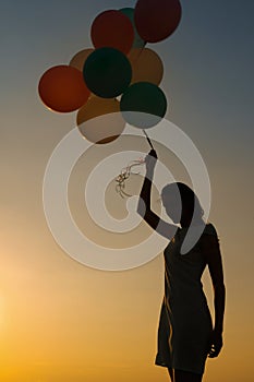Silhouette of young woman with flying balloons against the sky.