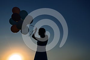 Silhouette of young woman with flying balloons against the sky.