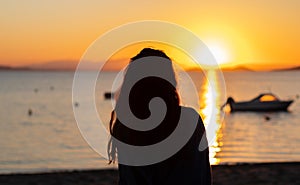 Silhouette of a young woman in front of a sunset on the beach, with boats and mountains. Vacation relax scene in Mar Menor, Murcia