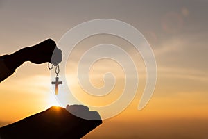 Silhouette of young woman hands holding holy Bible and lift of christian cross with light sunset background