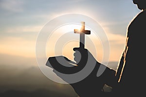 Silhouette of Young woman hands holding holy Bible and lift of christian cross, religion symbol in light and landscape over a