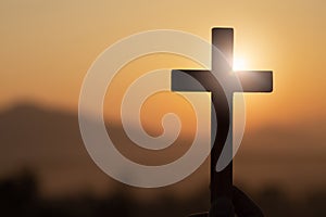 Silhouette of young woman hands holding lift of christian cross with light sunset background