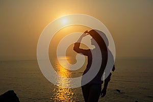 Silhouette of young woman in a hat against sunset over the sea. Beautiful slender girl enjoys peace and relaxation on the ocean