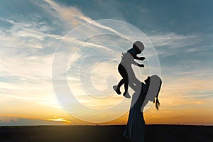 Silhouette of young woman high toss up little cute child baby boy on nature, sunset horizon background. Mother throw up