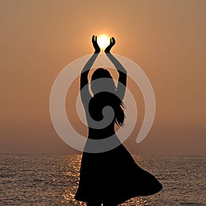 Silhouette of young woman holding the sun in her hands