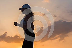 Silhouette of young woman jogging in the sport clothes on the sunset sky backgrounds. The concept of healthy lifestyle.