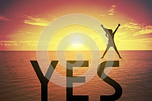 Silhouette young woman jumping and raising up her hand about happy concept on YES text over a beautiful sunset or sunrise
