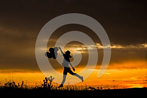 Silhouette of a young woman jumping at sunset. Outdoors. She is holdings balloons. Fun and lifestyle